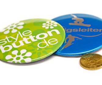 2 Stück 76 mm Buttons liegen zum Größenvergleich neben einer 50 Cent Münze